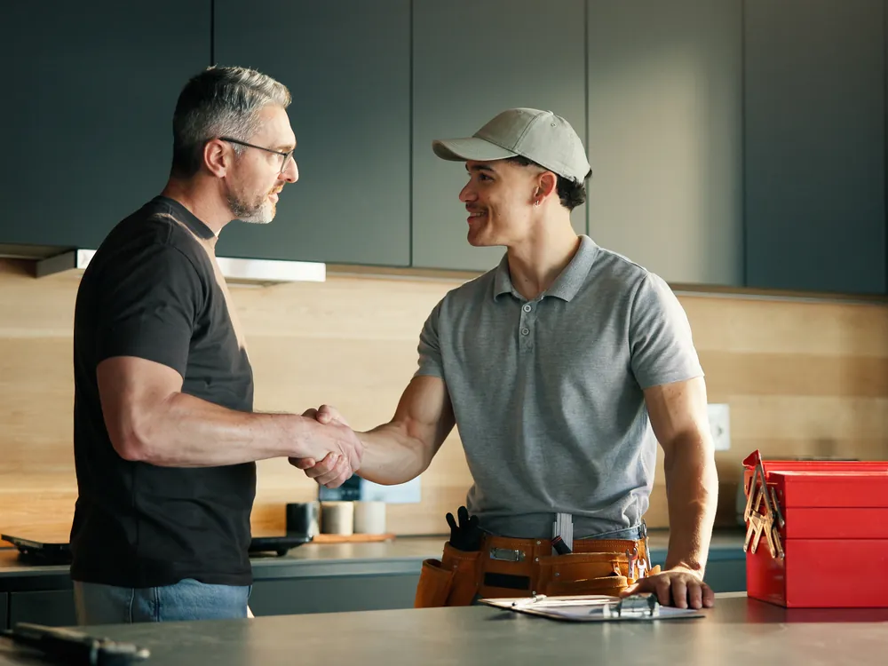 Handwerker und Kunde geben sich in einer Küche die Hand