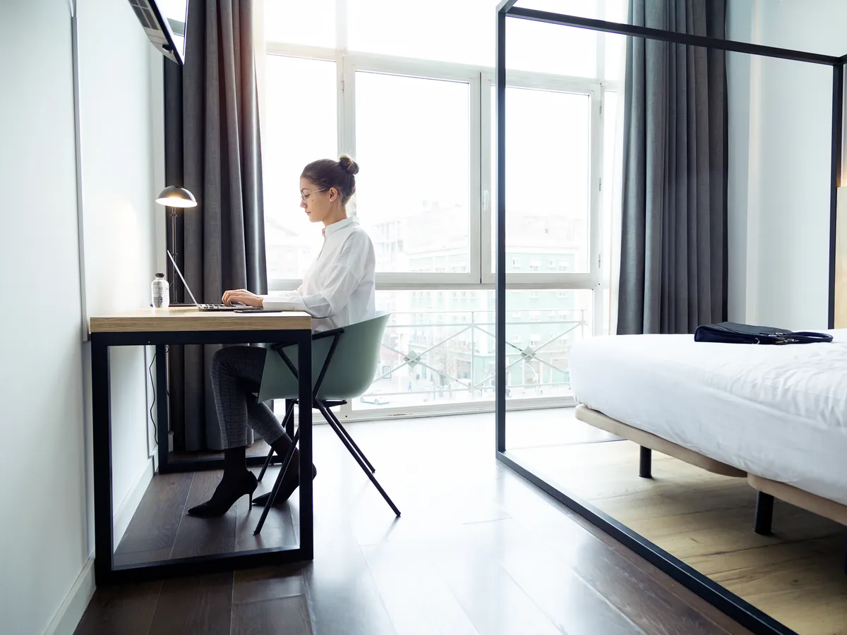 Gast sitzt am Schreibtisch eines Hotelzimmers am Laptop und bucht online