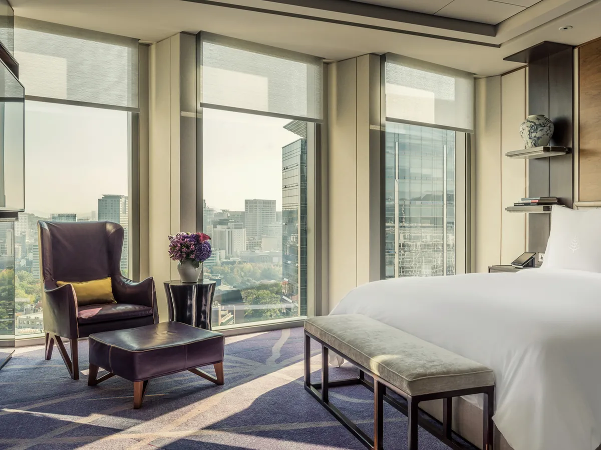 Helles Hotelzimmer mit grossem Fenster, Sesseln und Blick ueber die Stadt