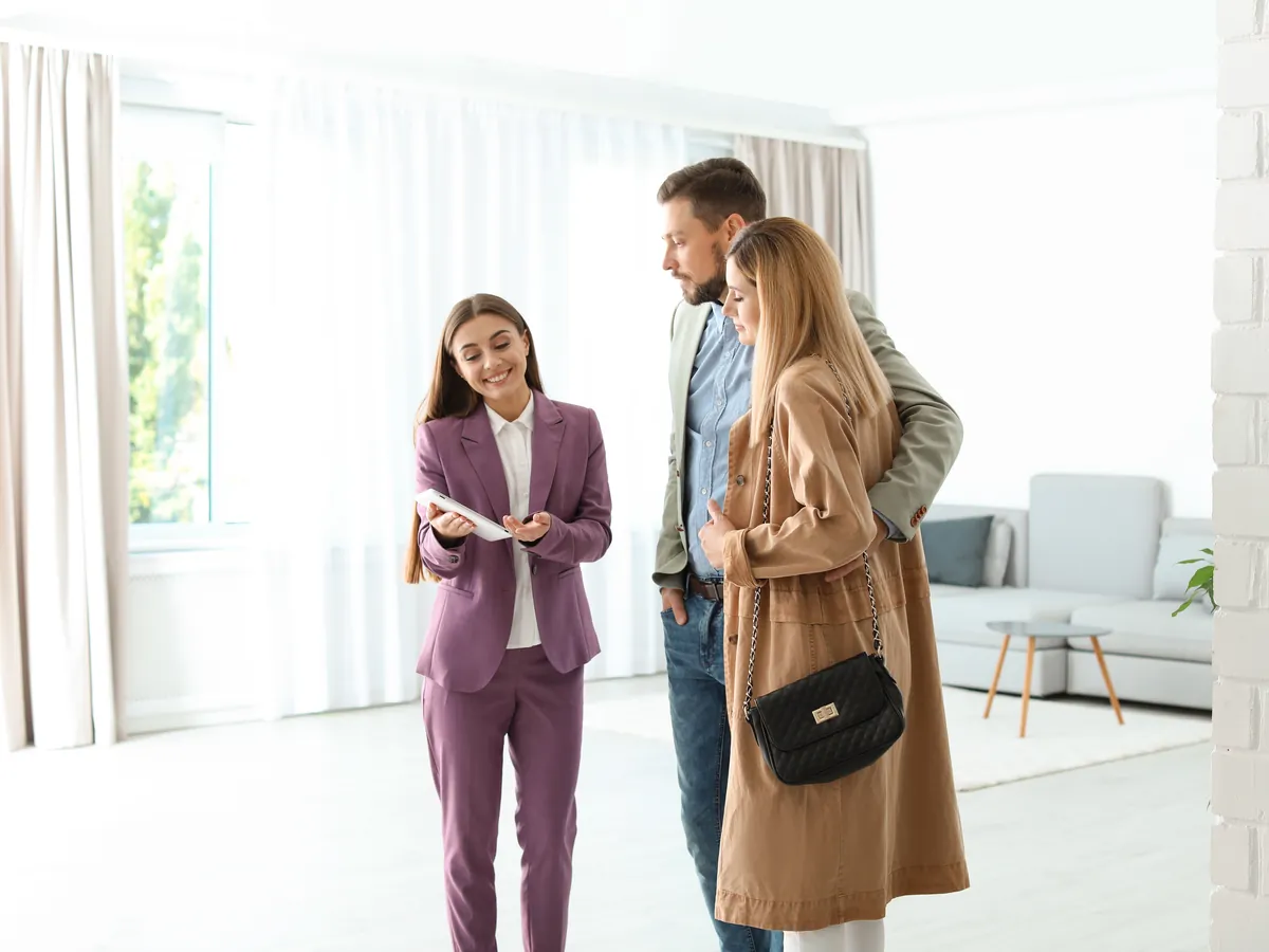 Immobilienmaklerin bespricht mit einem Paar Unterlagen in einer leeren, hellen Wohnung