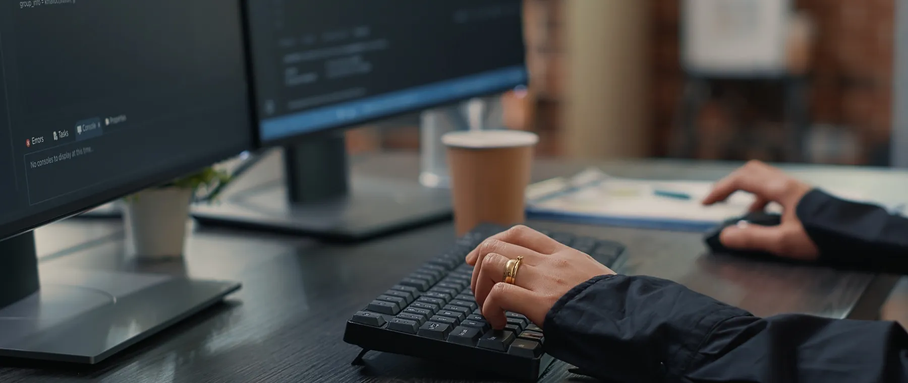 Naheinstellung: Hände tippen Code auf einer Tastatur vor zwei Monitoren mit Entwicklungsumgebung