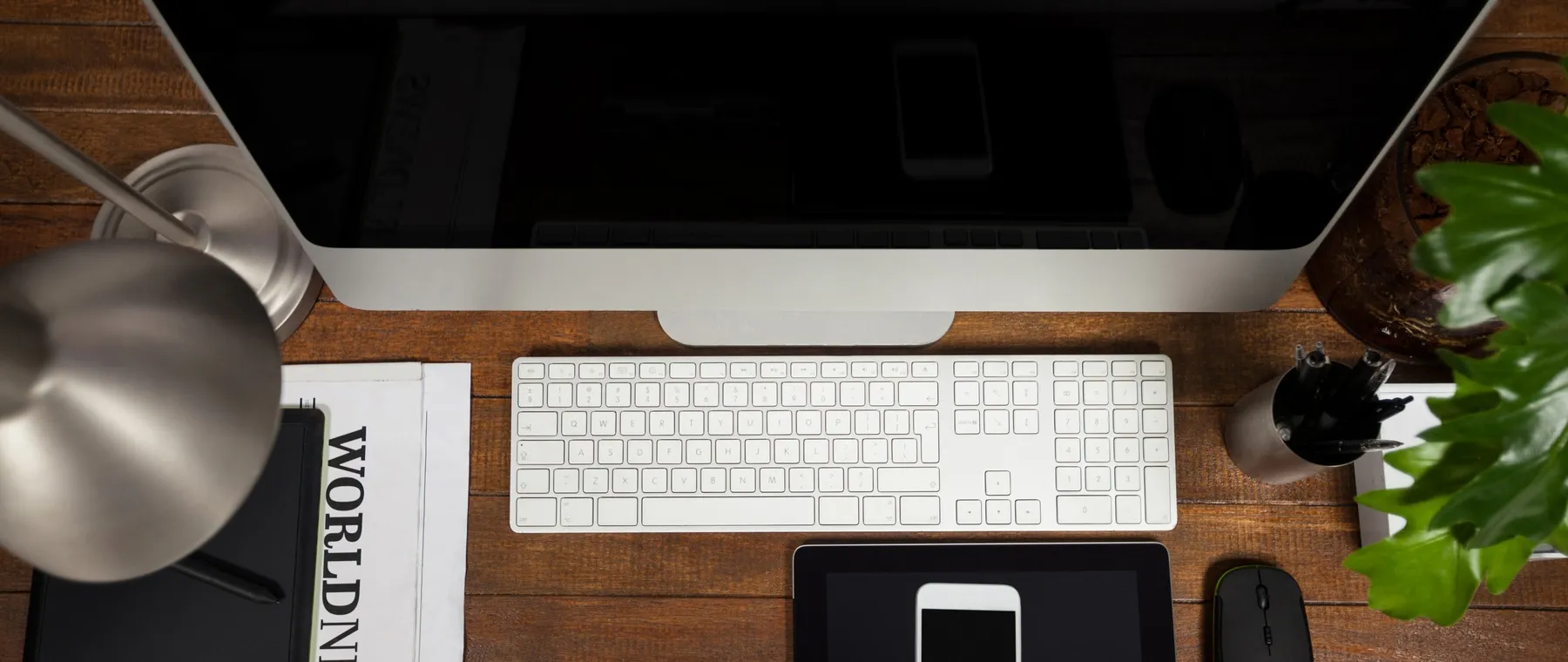 Aufsicht auf einen aufgeräumten Schreibtisch mit Rechner, Tastatur, Tablet und Notizblock