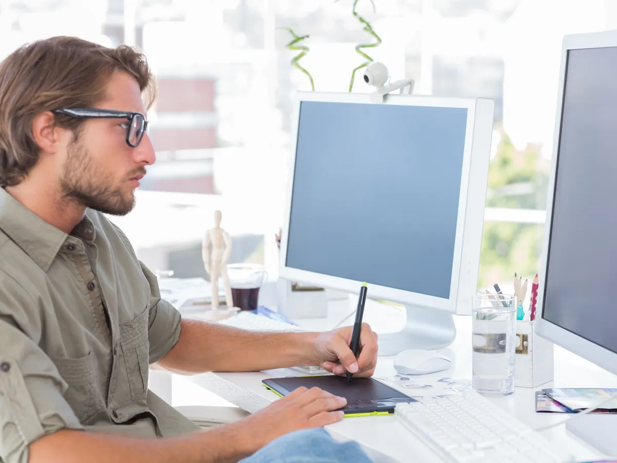Designer arbeitet an einem hellen Schreibtisch mit Grafiktablett und Monitor an einem Layout