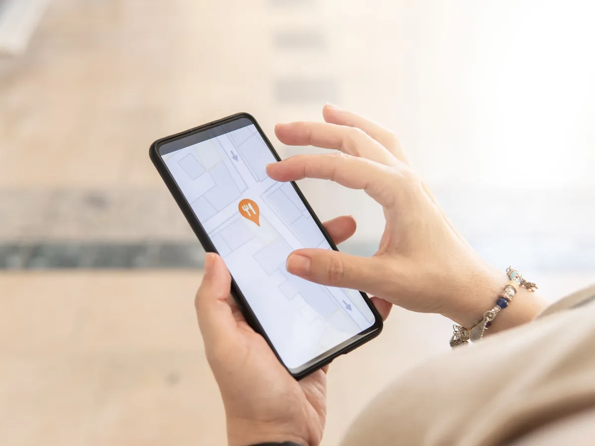 Hand haelt ein Smartphone, auf dem eine Karte mit einem markierten Standort zu sehen ist
