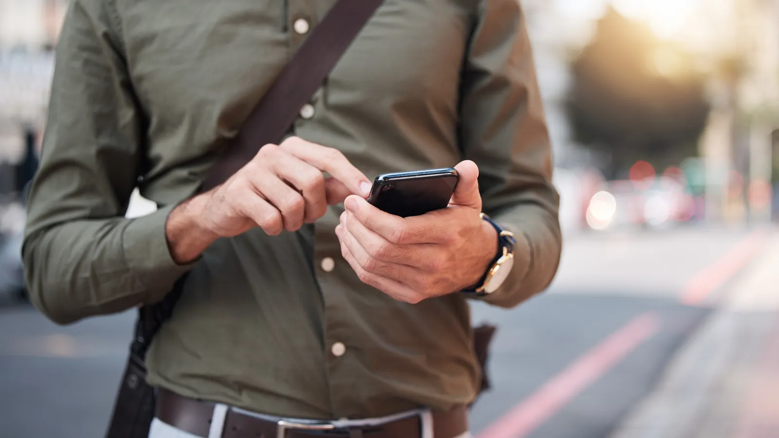 Mann tippt unterwegs auf einer Strasse etwas in sein Smartphone ein